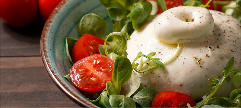 Burrata garnished with tomatoes and greens in a bowl.